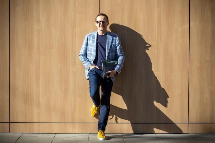 Professor Marek Kowalkiewicz, leaning against a wooden wall in his trademark yellow sneakers